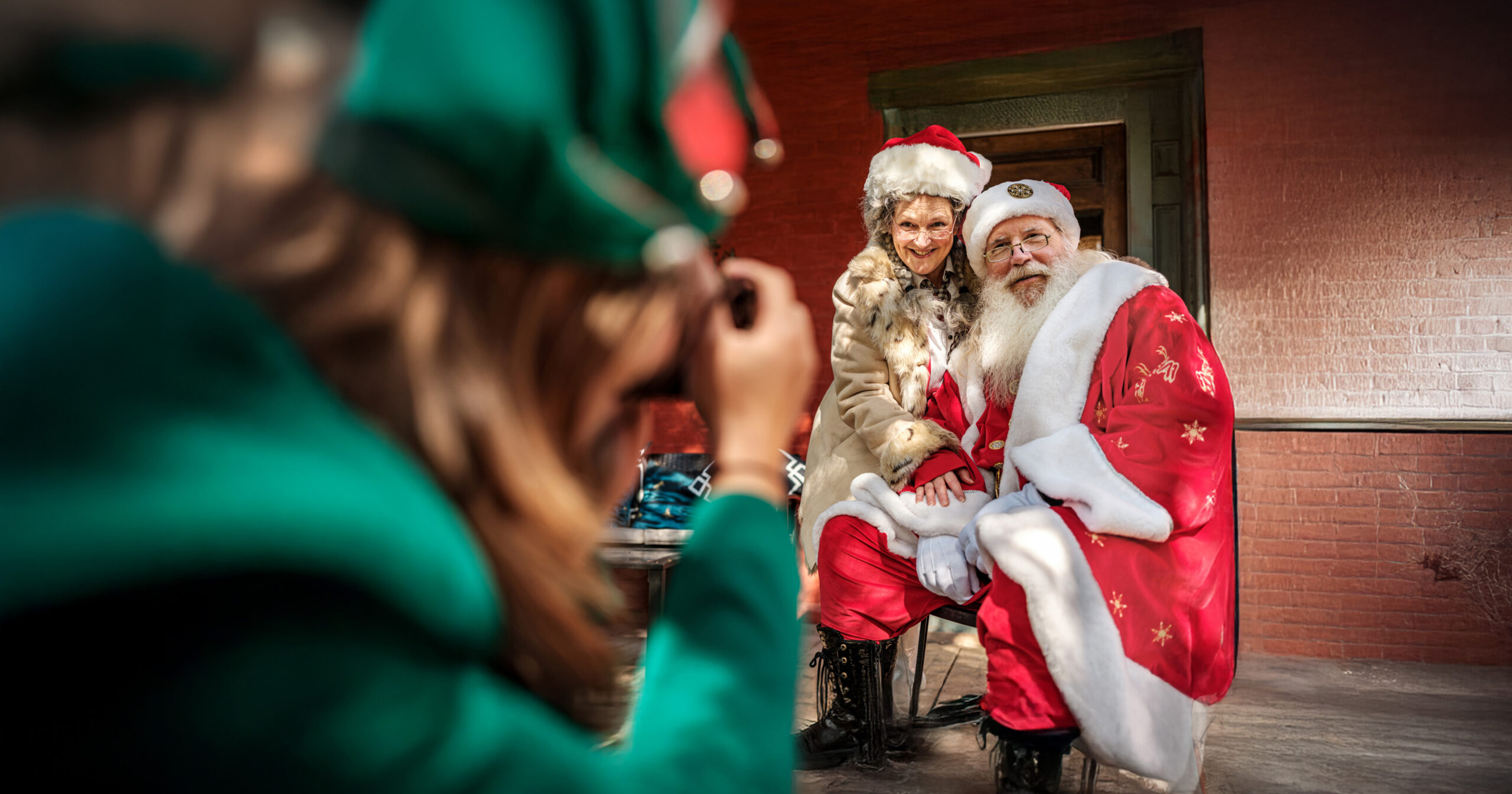 a woman dressed as an elf taking a photo of a senior woman in a santa hat with Santa Claus